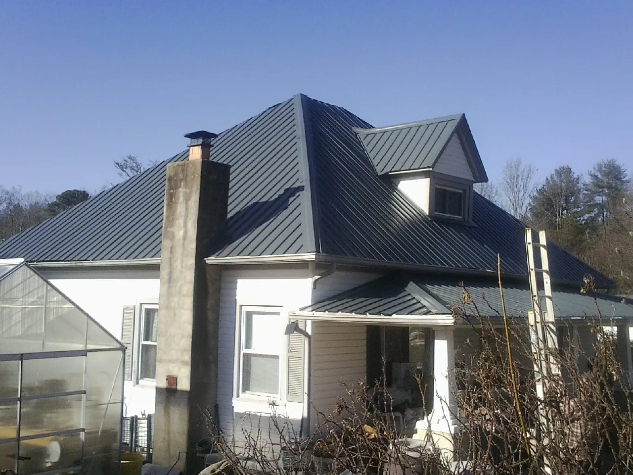 Dark blue standing seam metal roof on a white farmhouse with dormer — Slate & Tile Roof Repair by Roofing Brothers in Ann Arbor