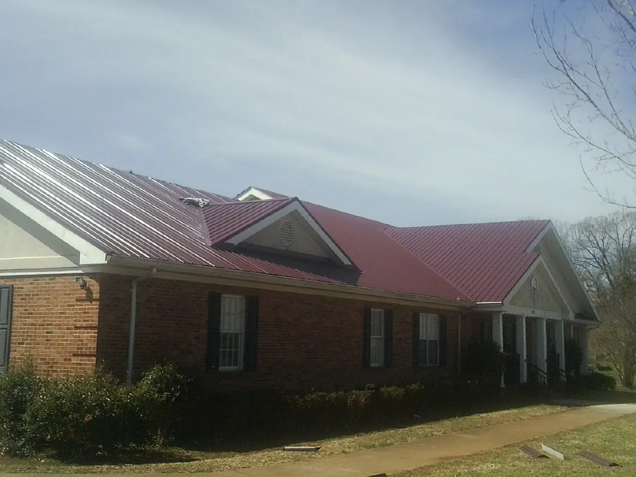 Red metal roof with gabled entries on a long brick building, from a Hail Damage Roof Repair job in Ann Arbor