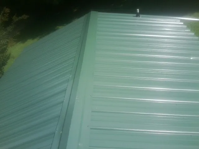 New green metal panels meeting at the ridge of a roof — Flat Roof Repair work by our crew in Ann Arbor