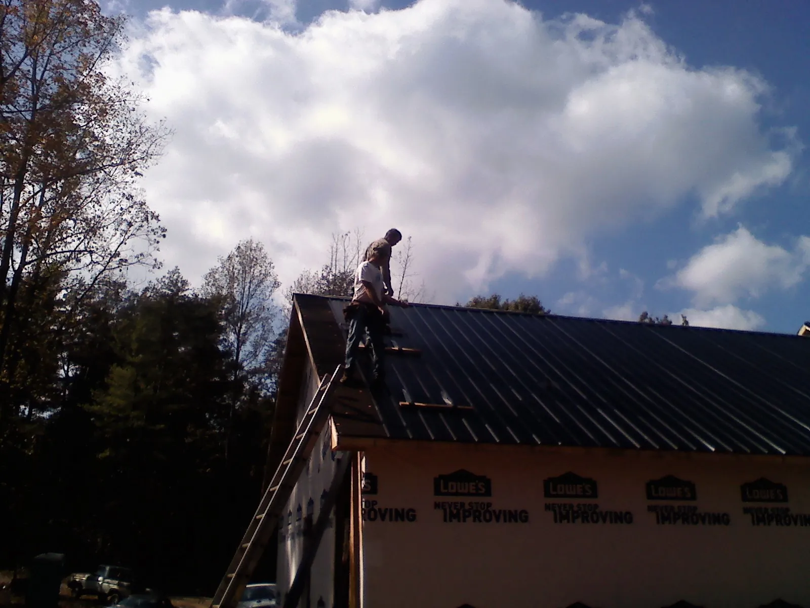 Roofer fastening dark metal panels high against a cloudy sky, from a Roof Inspection job in Ann Arbor